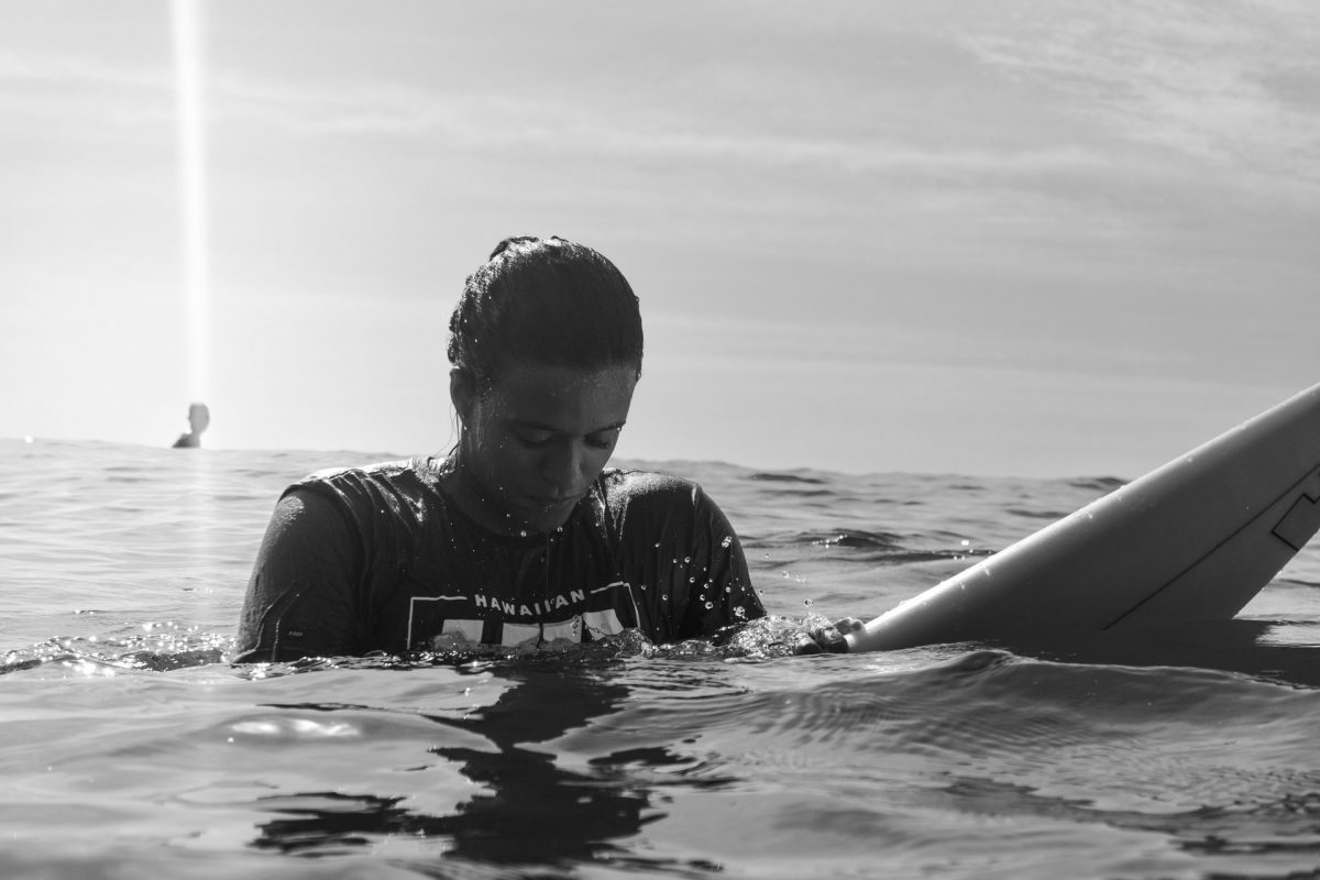 Surfista Julia Santos sentada sobre a prancha no mar